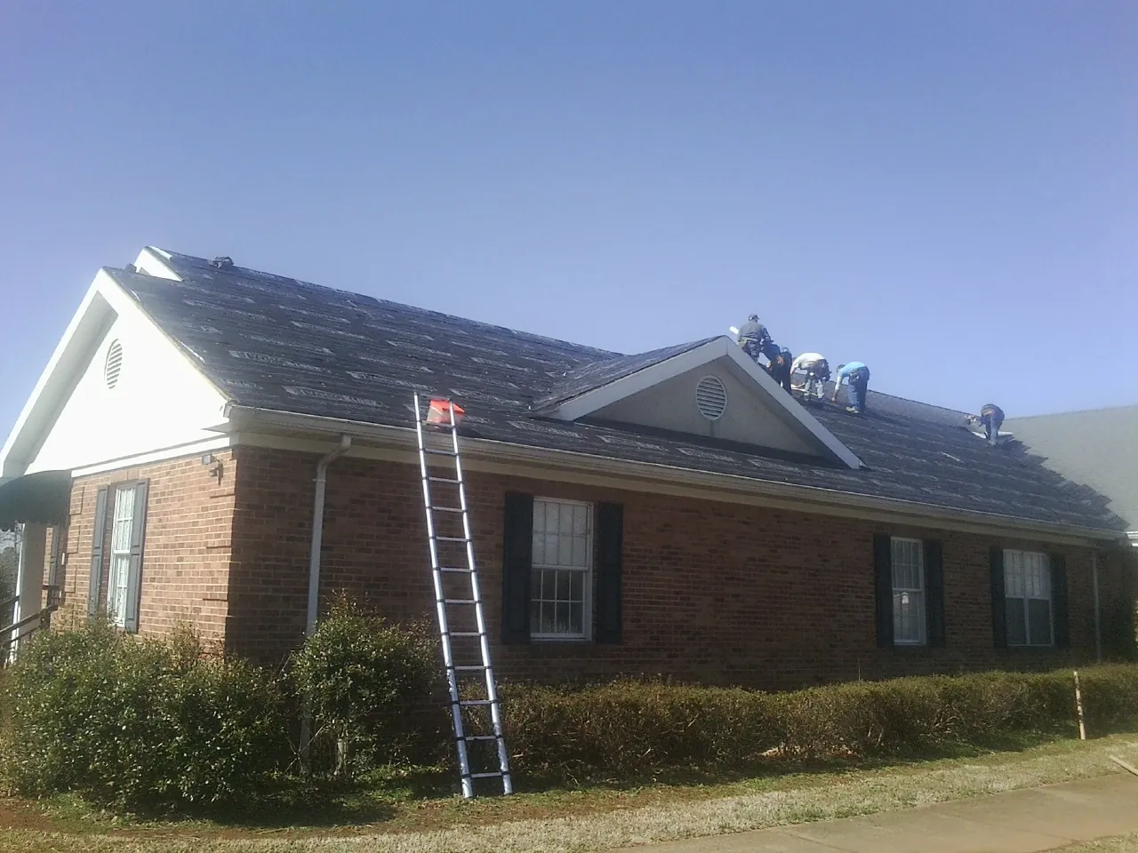 Crew tearing shingles off a brick ranch roof with a ladder set — Metal Roof Repair work by our crew in Carson