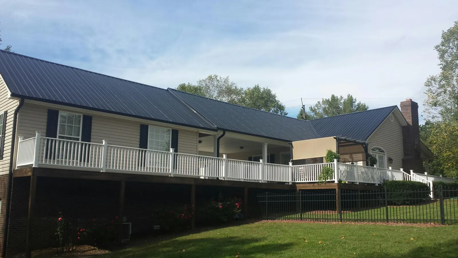 Black metal roof above a long white railed deck on a hillside home in Carson
